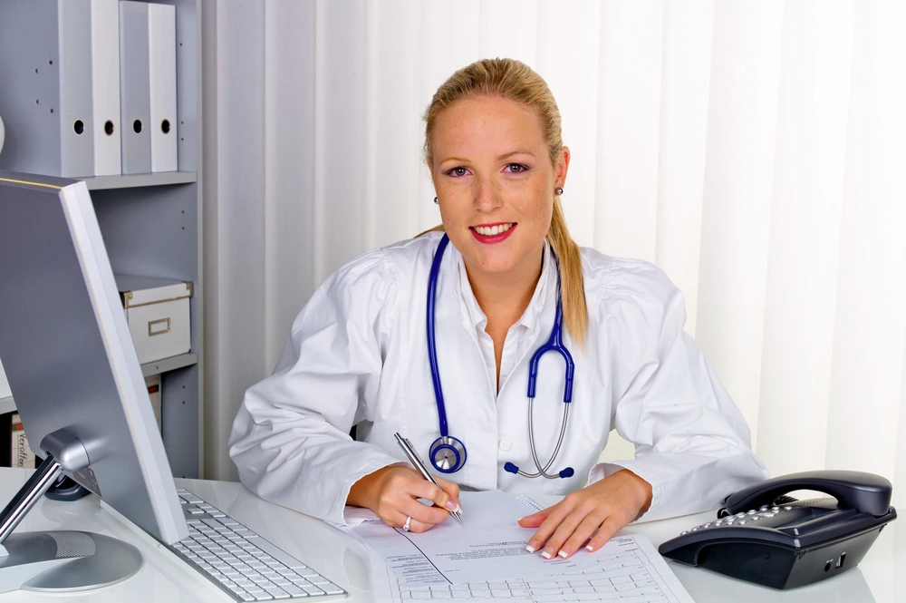 Smiling female doctor with a stethoscope writing at a desk