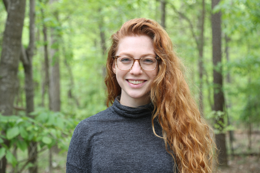 Portrait of a smiling woman with long red hair and glasses in a gray sweater